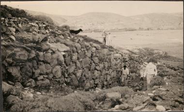 Melos. People climbing up hill with farmers and dog watching.