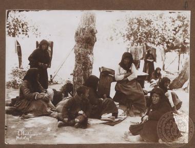 Εξαθλιωμένες γυναίκες και παιδιά (πιθανότατα πρόσφυγες) αναπαύονται σε υπαίθριο χώρο.