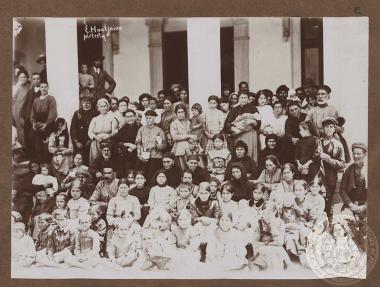 Ηλιιωμένοι, άνδρες, γυναίκες και παιδιά (πιθανότατα πρόσφυγες) έξω από κτίριο.