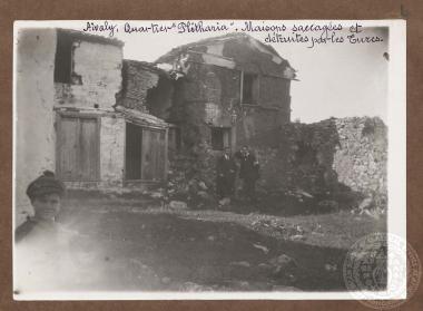 Δύο άνδρες όρθιοι μπροστά από κατεστραμμένα και ερειπωμένα σπίτια της συνοικίας 