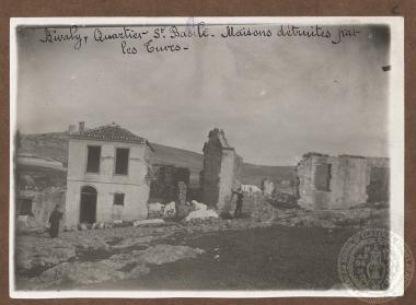 Ιερέας και ιατρός, ταρυματιοφορέας ή νοσοκόμος με περιοβραχιόνιο του ερυθρού σταυρού όρθιοι μπορστά από κατεστραμμένα και ερειπωμένα σπίτια της συνοικίας 