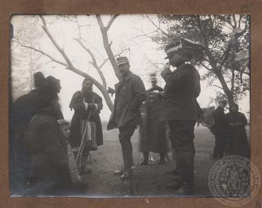 Ο Βασιλιάς Κωνσταντίνος (1868 - 1923) συνομιλεί με βοσκούς και παιδιά, συνοδευόμενος από αξιωματικούς, μέλη της συνοδείας του.