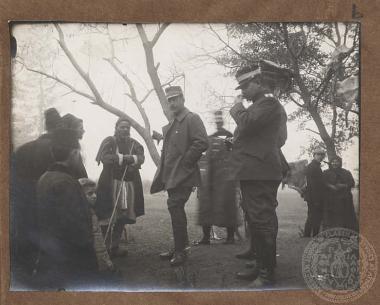 Ο Βασιλιάς Κωνσταντίνος συνομιλεί με βοσκούς και παιδιά, συνοδευόμενος από αξιωματικούς, μέλη της συνοδείας του.