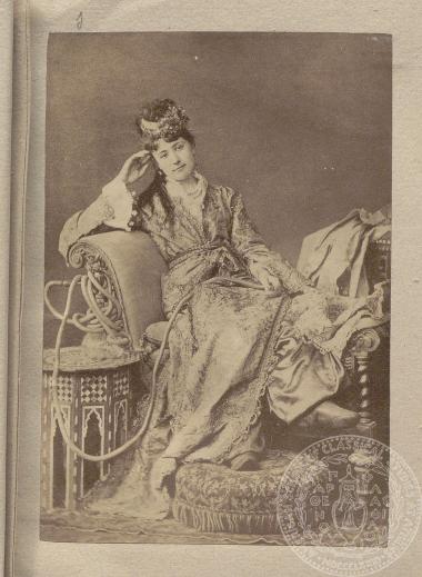 Γυναίκα πολυτελώς ενδεδυμένη, καπνίζει καθισμένη σε πολυθρόνα. Φωτογραφία της εποχής σε studio.