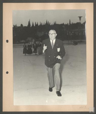 Επαμεινώνδας Πετραλιάς  στο Παναθηναϊκό Στάδιο.  Συνοδεύεται από κοπέλες του Λυκείου των Ελληνίδων με παραδοσιακές φορεσιές. Με τη στολή της Σκοπέλου η Φάνη Πάλλη-Πετραλιά