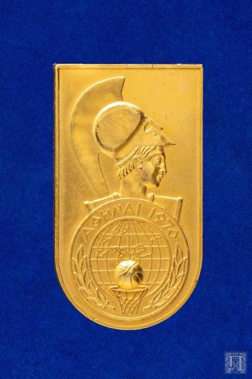 Αναμνηστικό μετάλλιο με παράσταση κεφαλή Αθηνάς και την επιγραφή ΑΘΗΝΑ 1970 γύρω από στεφάνι ελιάς μέσα στο οποίο εικονίζεται καλάθι μπάσκετ