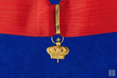 Κόκκινη γκρο κορδέλα με μία κορώνα από κράμα χαλκού με μεγάλο κρίκο η οποία προφανώς αποτελούσε το ενδιάμεσο συνδετικό διακοσμητικό μέσο