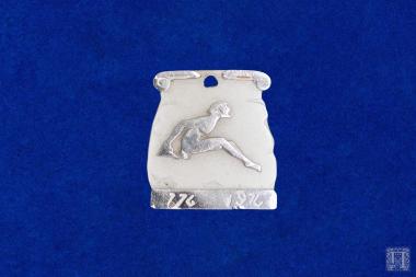 Αργυρή πλακέτα με οπή ανάρτησης και παράσταση αθλητή. Στο κάτω μέρος της φέρει αριστερά και δεξιά αντίστοιχα, εγχάρακτη επιγραφή 176 και 1970Στην οπίσθια όψη φέρει δύο χτυπήματα της καθαρότητας του κράματος