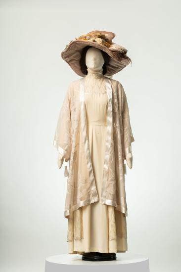 Γυναικείο φόρεμα μακρύ από τρεβίρα και τούλι, με τουνίκ από οργάντζα και σατέν. Συνοδεύεται από καπέλο από βελούδο