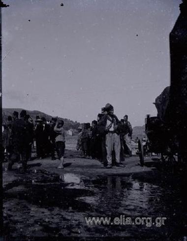 Turkish officials and civilians, among them lots of children, gathered at the pier. On the right, parked carriages.