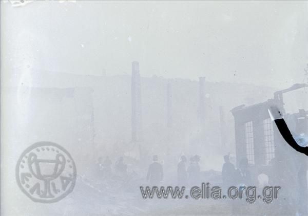 Άνδρες περπατούν ανάμεσα σε κτίρια κατεστραμμένα από φωτιά.