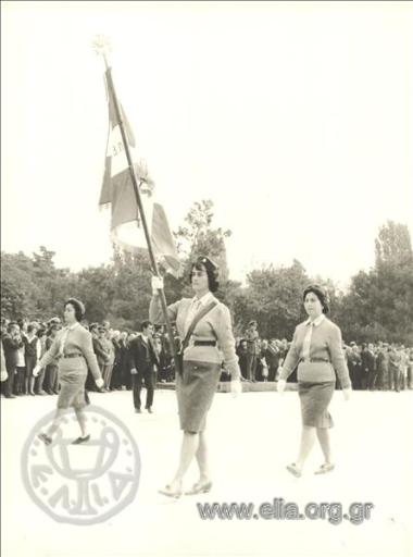 Σημαιοφόρος και δύο μαθήτριες παρελαύνουν.