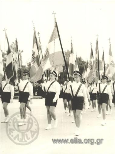 Μαθητές με σημαίες παρελαύνουν.