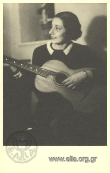 Η Αμαλία Φλέμινγκ με σχολική ποδιά παίζει κιθάρα.
