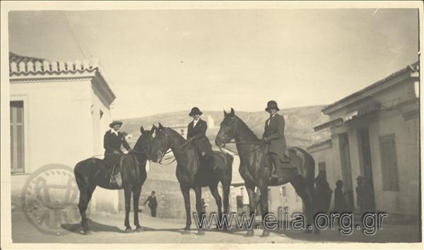 Three women on horseback on a street of a settlement in the area of Vouliagmeni.