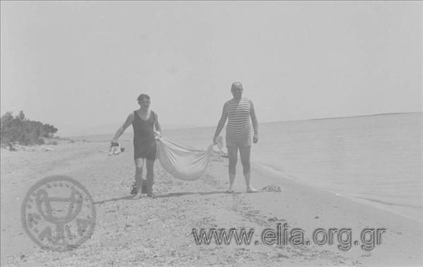 Ο Γιώργος Βαφιαδάκης με φίλο του κουβαλάνε πράγματα στην παραλία.