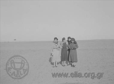 Παρέα γυναικών ποζάρει στην έρημο στην Heliopolis. Heliopolis: προάστιο του Καΐρου. Κατασκευάστηκε κατ' εντολή της εταιρείας Cairo Electric Railways & Heliopolis Oases Company, βελγο-αιγυπτιακών συμφερόντων. Εμπνευστής του έργου ο Βέλγος Édouard Empain. Η πόλη χτίστηκε μεταξύ 1907 και 1910 σε τμήμα ερήμου, δέκα χιλιόμετρα από την πόλη του Καΐρου.