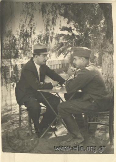 Stefanos G. Streit (Reserve Cadet) conversing with a man in an outdoor coffee house.