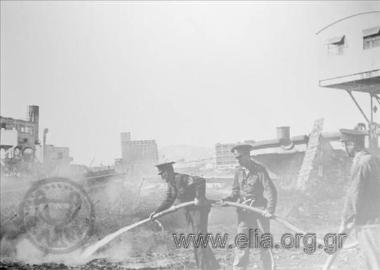 Άνδρες της Πυροσβεστικής Υπηρεσίας Πειραιά προσπαθούν να σβήσουν φωτιά στο λιμάνι, μετά το βομβαρδισμό από τις αποχωρούσες γερμανικές δυνάμεις κατοχής.