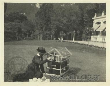 Μία από τις θείες του Νικόλαου Τομπάζη ταίζει νεαρός άνδρας που βρίσκεται μέσα σε κλουβί ωδικών πτηνών.