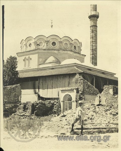 Man in front of mosque standing among buildings reduced to rubble