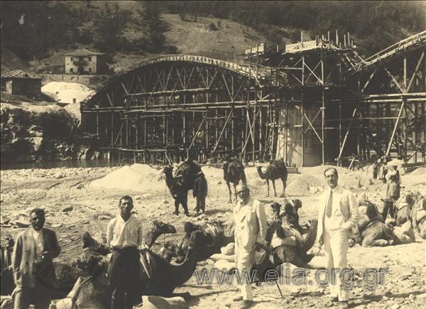 The construction of the bridge at Nestos river. The contractors (?) pose  on camels in the riverbed, with the bridge as a background.