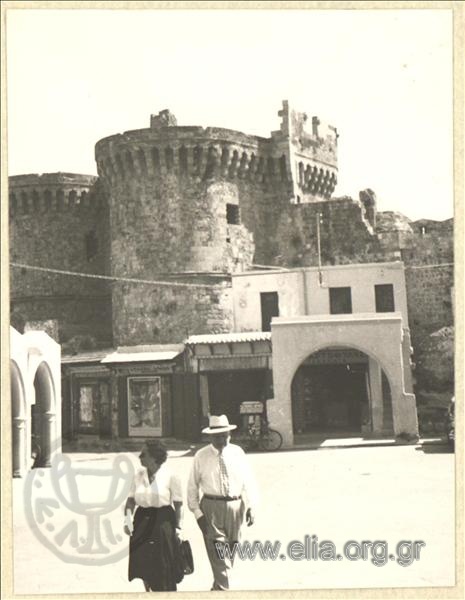 A couple walking. Towers and part of the medieval walls of Rhodes.