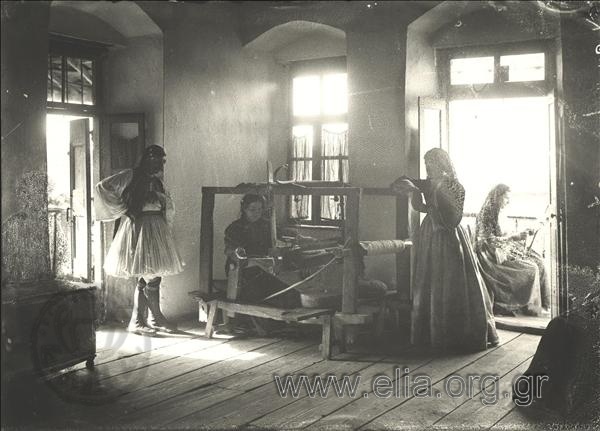Εσωτερικό σπιτιού, αργαλειός, φουστανελλοφόρος και τρεις γυναίκες με παραδοσιακές ενδυμασίες.