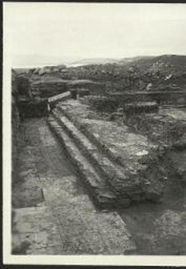 Το νότιον βάθρον των εδράνων των κληρικών. Εις το βάθος αριστερά μεταγενέστερος τοίχος και παραπλεύρως η μαρμαρίνη πλίνθος του κίονος του ΝΑ διπλού στηρίγματος. Όπισθεν των εδράνων υψηλός στηλοβάτης.