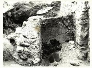 Τομέας Δ, πρώτος όροφος, Δωμάτιο Δ13. Το ερμάριο στη ΒΑ γωνία, δίπλα στη θύρα για το δωμάτιο Δ12. Πίσω από τον πλινθότοιχο του ερμαρίου διακρίνεται πίθος από το Δωμάτιο Δ11. (Thera IV, πίν. 49a).