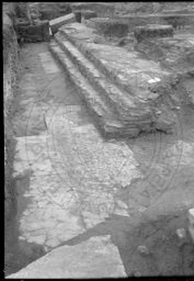 Το νότιον βάθρον των εδράνων των κληρικών. Εις το βάθος αριστερά μεταγενέστερος τοίχος και παραπλεύρως η μαρμαρίνη πλίνθος του κίονος του ΝΑ διπλού στηρίγματος. Όπισθεν των εδράνων υψηλός στηλοβάτης.