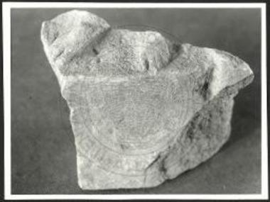 Πλίνθος αναγλύφου διασώζουσα τα κάτω μέρη των ποδών ισταμένου προσώπου.