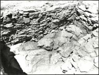 Η παρειά Ζ εις τον κεντρικόν τομέα της τάφρου FW6 από ΝΑ. Πλησίον του ακοντίου ο φυσικός βράχος υπό το δέκατον τρίτον στρώμα εις το τέλος της ανασκαφής του τομέως.