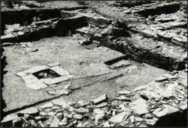 Δωμάτιον 19. Άποψις από Βορρά. Διακρίνεται η μεγάλη κεντρική εστία και εν σκαφοειδές δοχείον πλησίον του δυτικού τοίχου.