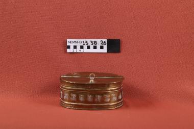 Κουτί - κουτί χάλκινο ωοειδές με καπάκι που ανοίγει στη μέση με ένωση μεντεσέ και εμπίεστη διακόσμηση με ανθικό μοτίβο περιμετρικά