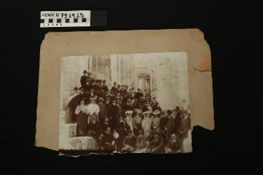Φωτογραφία - φωτογραφία ασπρόμαυρη που απεικονίζει ομάδα ανδρών και γυναικών που φορούν αστικά ενδύματα αρχών του 20ού αι. και ποζάρουν στα κατάλοιπα αρχαιοελληνικού ναού. Επικολλημένη σε χαρτόνι γκρι