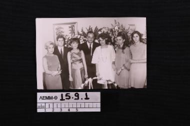 Φωτογραφία - φωτογραφία ασπρόμαυρη που απεικονίζει δύο άνδρες και πέντε γυναίκες (η μία είναι η δωρήτρια Χαρίκλεια Σάκκη) ντυμένες με φορέματα της δεκαετίας του 1960, που ποζάρουν με φόντο ανθοδέσμες και δύο κάδρα
