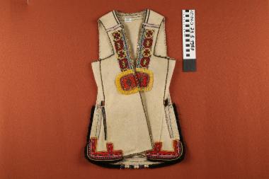 Επενδύτης - μάλλινος, αμάνικος, παιδικός σαγιάς, σε υπόλευκο χρώμα διακοσμημένο με κεντημένες υφαντές κορδέλες με σταυρόσχημα μοτίβα και μαύρα κρόσσια