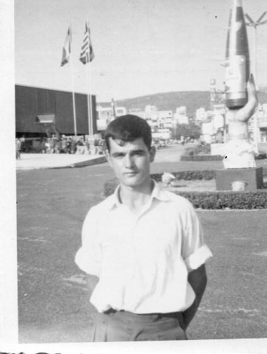 A young man is photographed in front of a pavilion at the Thessaloniki International Fair