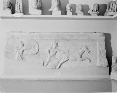 Μακρά πλευρά σαρκοφάγου με ανάγλυφη παράσταση άρματος και δύο πολεμιστών. Ο Αχιλλέας μπροστά από τα τείχη της Τροίας