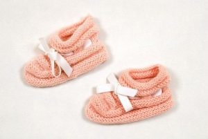 Pair of knitted pink baby shoes with bow tie.