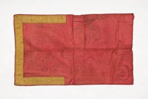 Piece of faded red silk edged with gold braid.