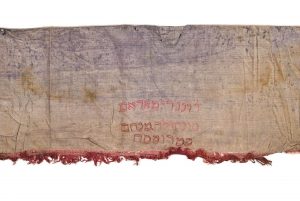 Bimah front decoration (?), worn velvet, edged at lower border with wine red fringe trim, embroiderd pink and brown inscription, donated by Sanhoula Menahem Stroumsa.