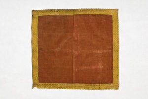 Piece of brown cloth edged with gold braid.