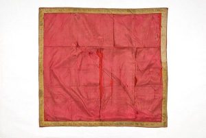 Piece of faded red silk edged with gold braid.