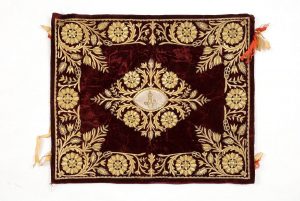 Dark red velvet with gold embroidery in couching technique, spiraled threads and sequins, central floral ornament, corner motifs and broad foliate border, beige ribbon ties at both ends.