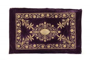 Eggplant violet velvet with gold embroidery in couching technique, spiraled threads and sequins, central floral ornament, corner motifs and foliate border, central applique inscribed with 'Stamo Abraham'.
