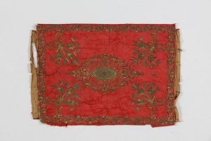 Red silk with laid and couched embroidery, central floral ornament, corner motifs and foliate border, ribbon ties at both ends, probably belonged to the local Jewish community.