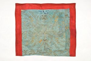 Cover for the reader's desk or Tik (Torah case) wrapper (?), light blue silk with gold floral embroidery, domestic textile in secondary use, bordered with red satin, dark blue embroidered inscription, dedicated in the name of Reina A