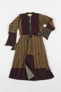 Coat dress with long sleeves partly covering the hands, violet, yellow and black striped cotton, bodice front, cuffs and lower part of skirt made of striped cotton in dark violet tones and embroidered with white and green thread, probably belonged to a member of the the local Jewish community.